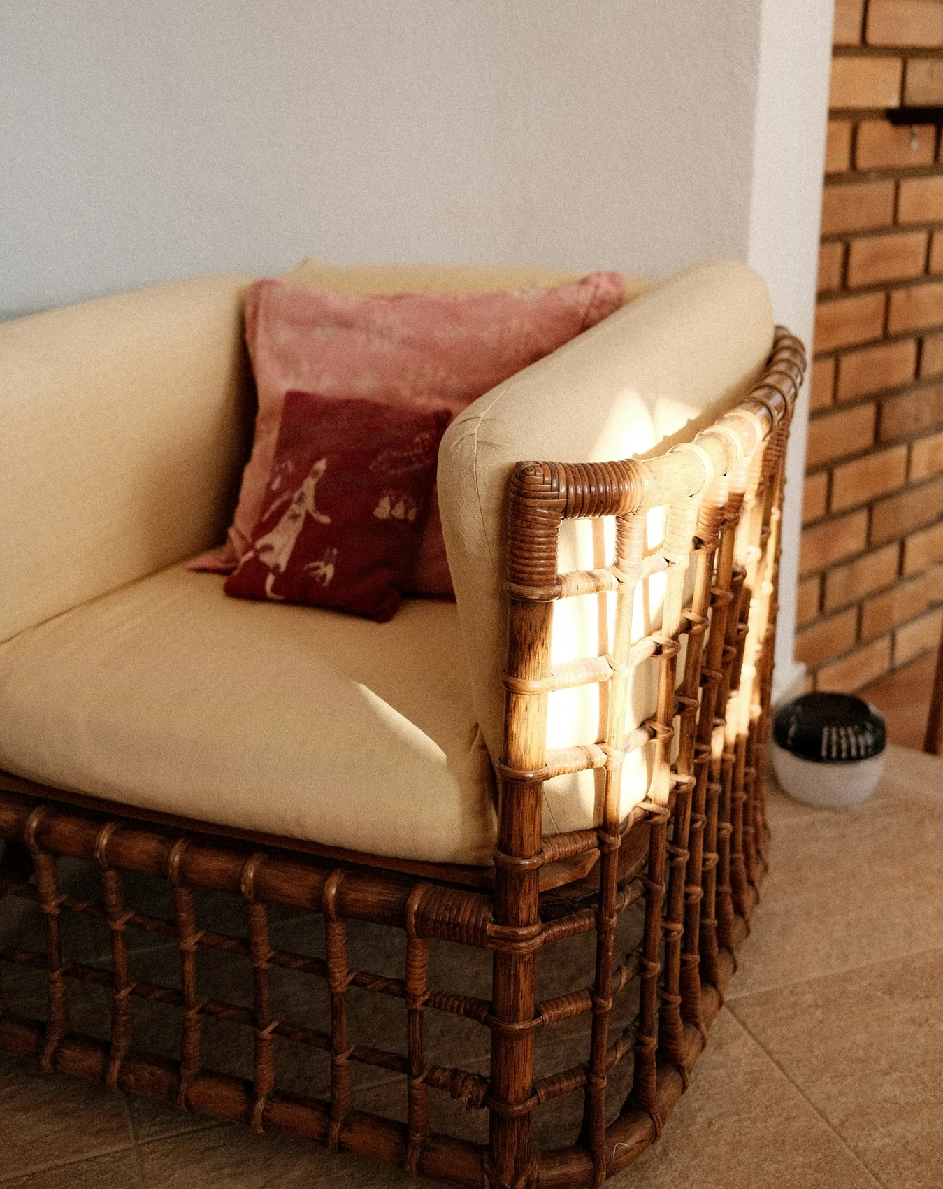 A sunlit wicker chair with cream upholstery and warm-toned cushions